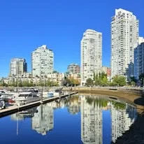 Glass residential towers reflected in the still water of a marina on a sunny day